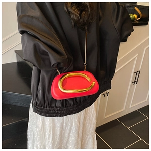 Detail of red leather crossbody bag featuring a distinctive gold curved metal buckle