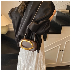 Detail of pill-shaped brown leather clutch with gold C-handle and snake chain strap