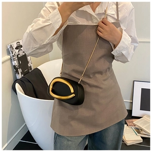 Detail of a matte black mini bag with a large gold oval metal buckle and chain strap