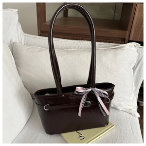 Detail einer dunkelbraunen Lederhandtasche mit Metallring und Schleifenanhänger
