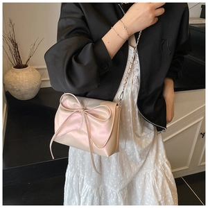 Close-up of light pink pearlescent crossbody bag with a large decorative bow and chain