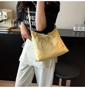 Detail of yellow nylon tote bag with knot decor and shoulder strap on model