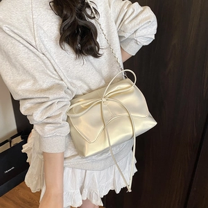 Elegant beige crossbody bag with large bow detail and metallic chain shoulder strap