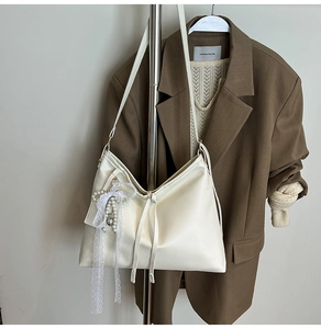 Detail of off-white leather tote bag featuring lace bow and elegant pearl charm