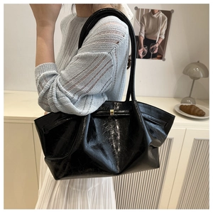 Detalle de bolso tote plisado negro brillante con detalles metálicos y correas finas