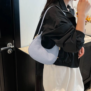 Minimalist light blue crescent hobo bag with denim texture and gold zipper worn by model