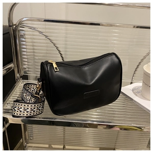 Detail of a black leather Boston bag with a patterned wide strap and gold hardware
