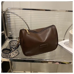 Detail of a brown leather Boston bag with a chic woven strap on a glass shelf
