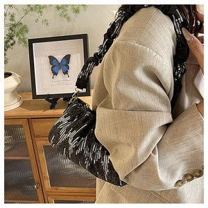 Détail du sac d'épaule à paillettes noires avec anse plissée et boucle dorée