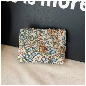 Detail of floral tapestry fabric texture and light gold chain on a crossbody bag