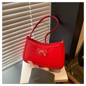 Detail of red crocodile pattern shoulder bag with a golden bow buckle in hand