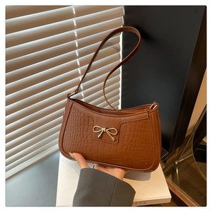 Close-up of brown crocodile embossed leather shoulder bag with gold bow buckle