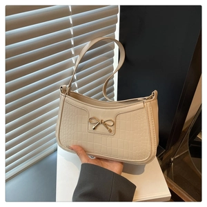 Detailed close-up of a cream-colored crocodile pattern bag with a gold bow accent