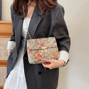 Floral embroidered crossbody chain bag with golden clasp over a grey blazer and white skirt