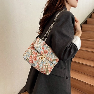 Floral print shoulder bag with gold chain strap worn over a dark grey blazer