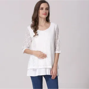 Detail of white lace maternity top showing hollow floral patterns and layered hemline