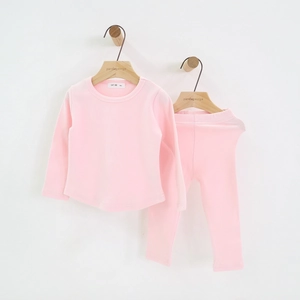Detail view of pink cotton kids' pajama set hanging on a minimalist wooden hanger