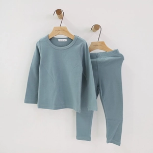 Kids long sleeve pajama set in greyish blue cotton hung on a wooden hanger on white wall