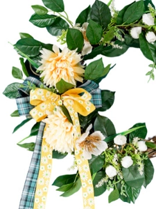 Detail of artificial Christmas wreath featuring green leaves, cream dahlias and festive bows