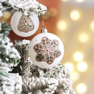 White Christmas ball ornament with red and green glitter snowflakes on snowy pine branch