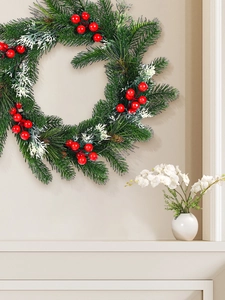 Detail of pine needle Christmas wreath with red berries and snow coating on a beige wall