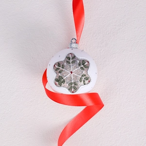 White Christmas ball with glitter snowflakes and red ribbon on festive background