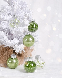 Close-up of green glitter and bead-filled clear Christmas ball ornaments on a snowy tree