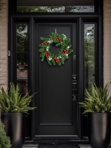 Christmas wreath with red berries and pine needles hanging on a modern black front door