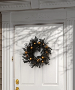 Close-up of a black Halloween wreath with gold and black ornaments on a white door