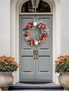 Close-up of pine cones and red ornaments on Christmas wreath hanging on a gray door