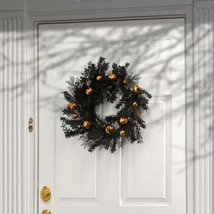 Elegant black Halloween wreath with gold ornaments hanging on white door