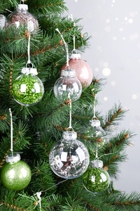 Close-up of assorted PET Christmas ornaments hanging on a green tree with bokeh background