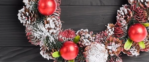 Macro detail of Christmas wreath with snowy pinecones and red ornaments on wood