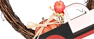 Detail of harvest wreath with red flowers, pumpkins, and a wooden truck on rattan