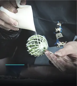 Detail of hand-drawn white patterns being applied to a green faceted Christmas ball ornament