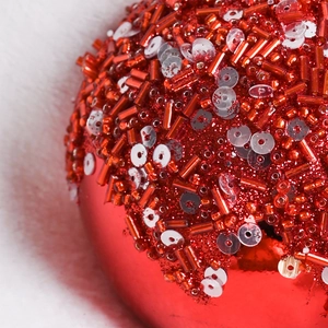 Red 8cm Christmas ball with glitter and beads on a soft white faux fur background