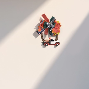 Fall harvest door wreath with maple leaves, plaid bows, and vintage truck on white wall