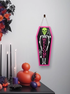 Pink coffin-shaped Halloween sign with skeleton and WELCOME text on a gray wall hooks