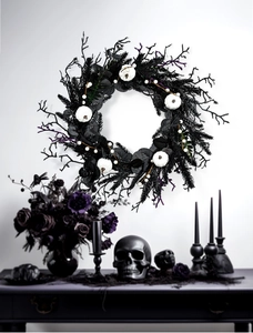 Detail of Halloween wreath with black pine needles and white mini pumpkins on a white wall