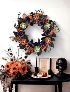 Detail of Halloween wreath with purple roses and orange spider web ornaments on white wall