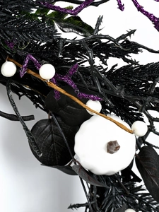 Detail showing white pumpkin, black leaves, and purple glitter branch on Halloween wreath