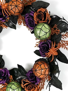 Detail of Halloween wreath with purple roses and orange glitter spiders on black leaves