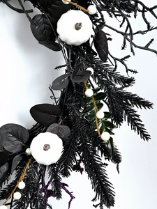 Detailed close-up of gothic wreath with black leaves, white pumpkins and purple glitter