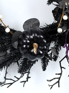Macro shot of black glossy pumpkin with gold stem and purple glitter on Halloween wreath
