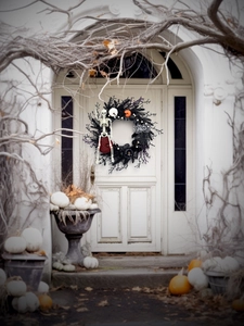Halloween wreath with skeleton and pumpkins hanging on a vintage white door