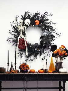 Close-up of Halloween wreath with skeleton, pumpkins and Happy Halloween sign on white wall