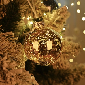 Sparkling gold Christmas ball ornament hanging on snowy pine branch with bokeh lights
