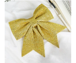 Detail of large glitter gold Christmas bow ornament on white fabric with a vintage book