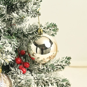 Polished silver Christmas ball ornament with gold string hanging on snowy pine branch