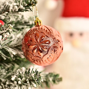 Rose gold Christmas ornament with embossed floral patterns hanging on a snowy tree